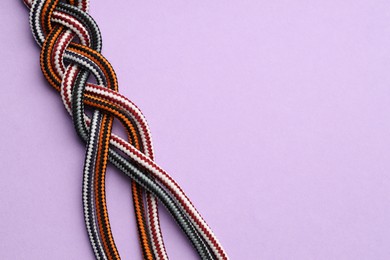 Photo of Braided colorful ropes on lilac background, top view with space for text. Unity concept