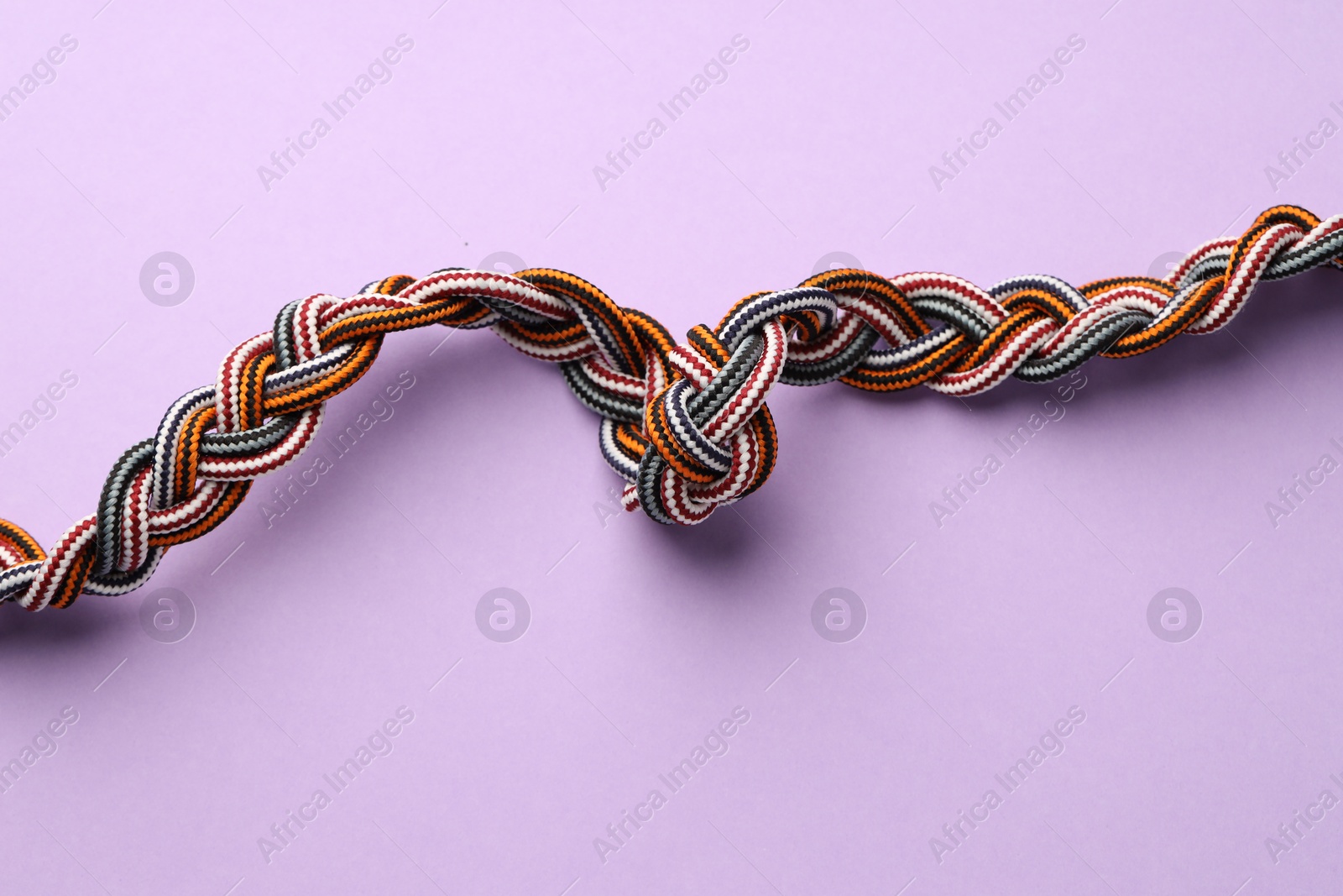 Photo of Braided colorful ropes on lilac background, top view. Unity concept