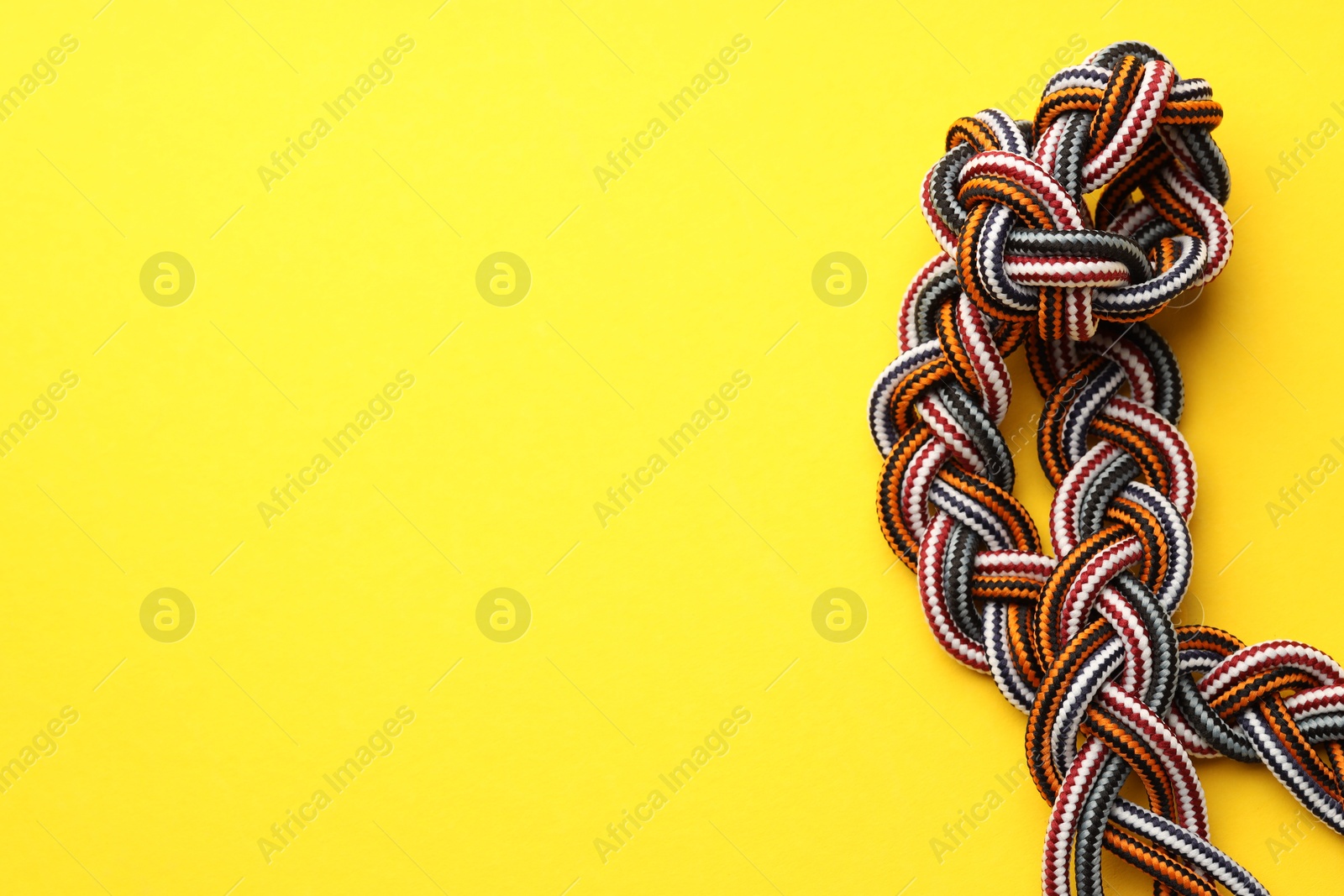 Photo of Braided colorful ropes on yellow background, top view with space for text. Unity concept