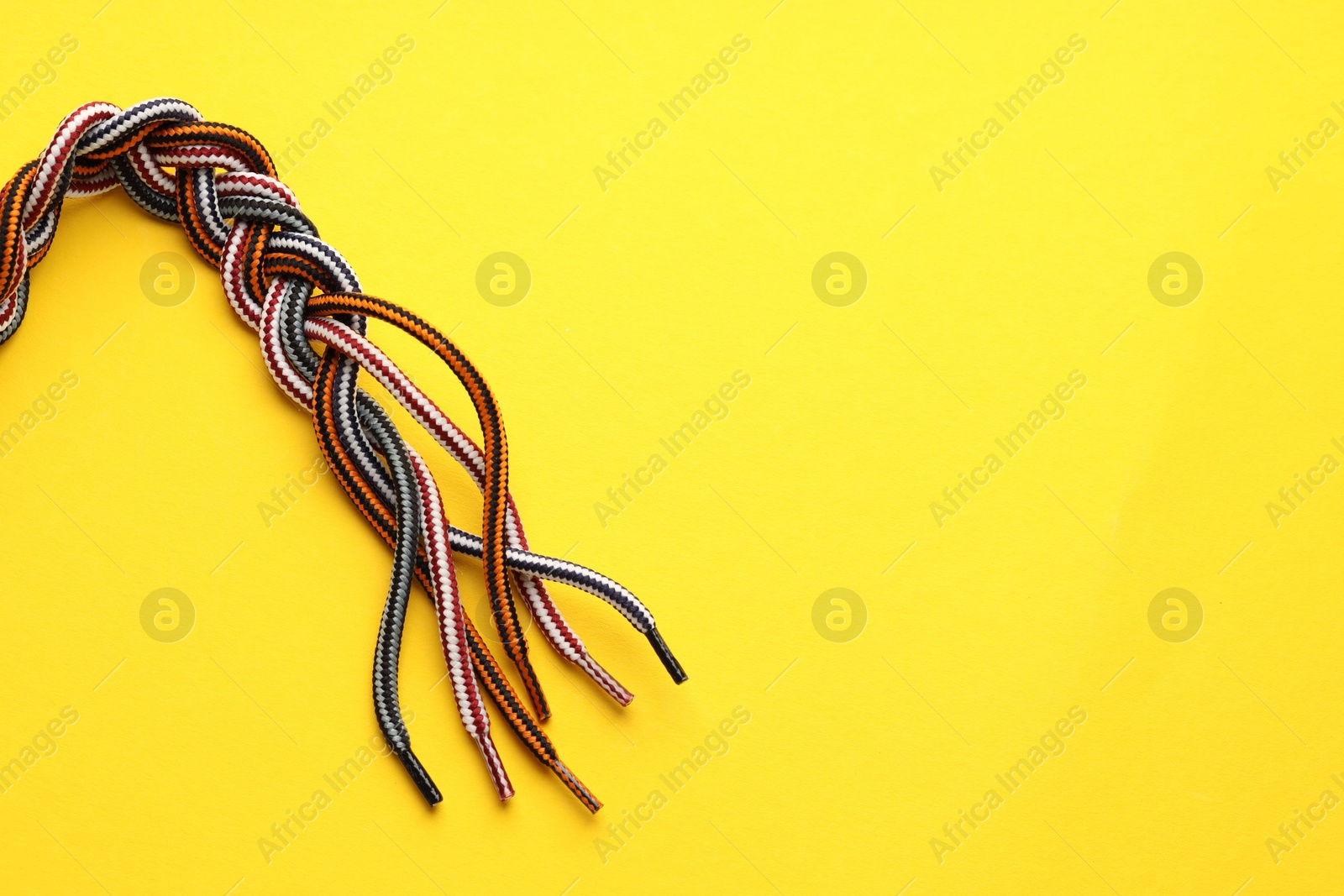 Photo of Braided colorful ropes on yellow background, top view with space for text. Unity concept