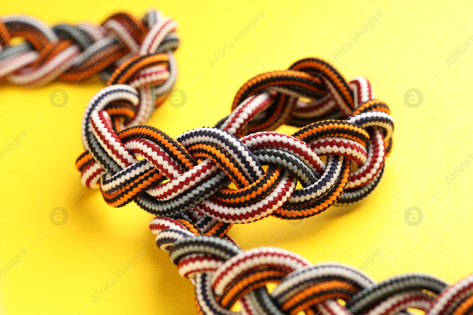 Photo of Braided colorful ropes on yellow background, closeup. Unity concept