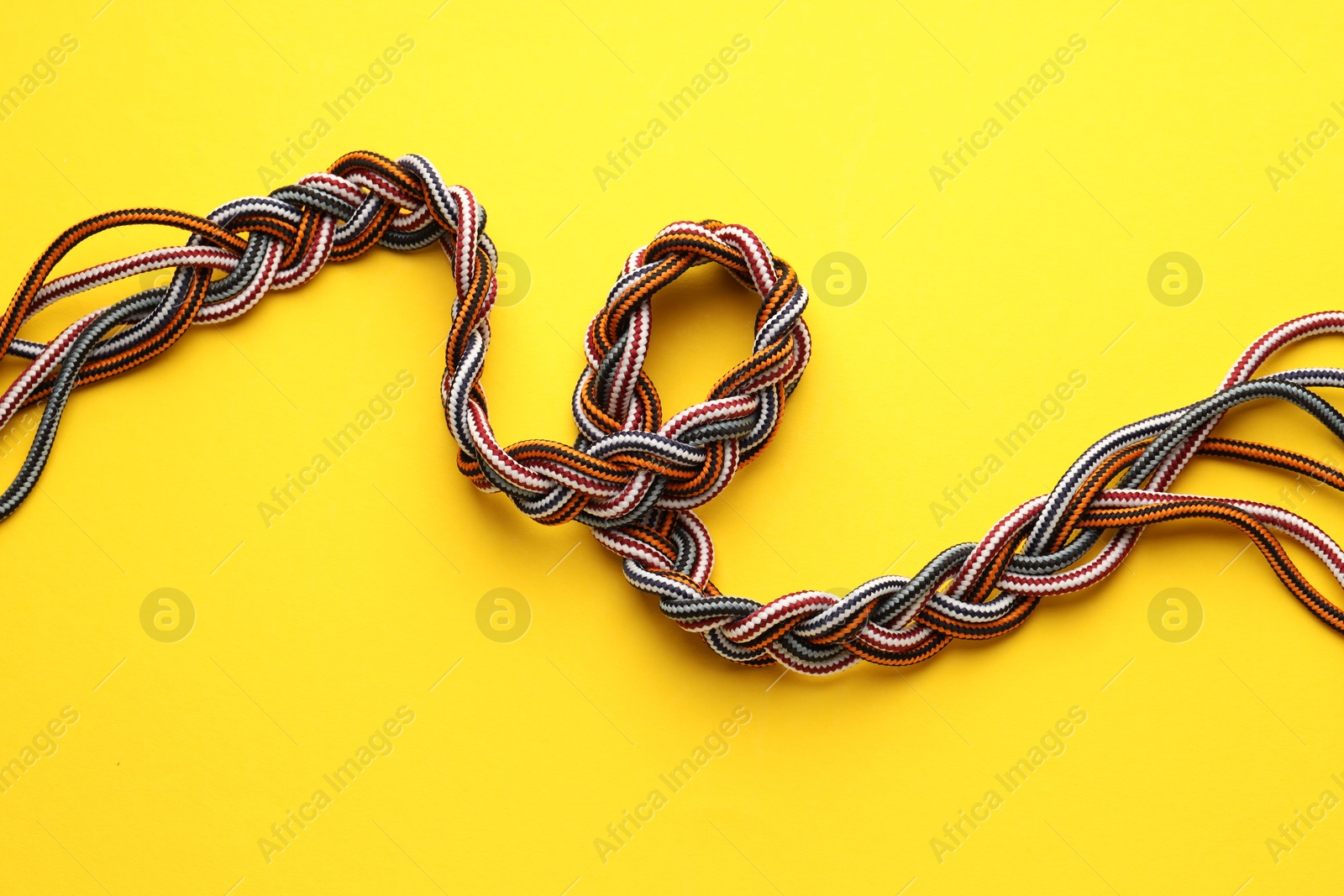 Photo of Braided colorful ropes on yellow background, top view. Unity concept