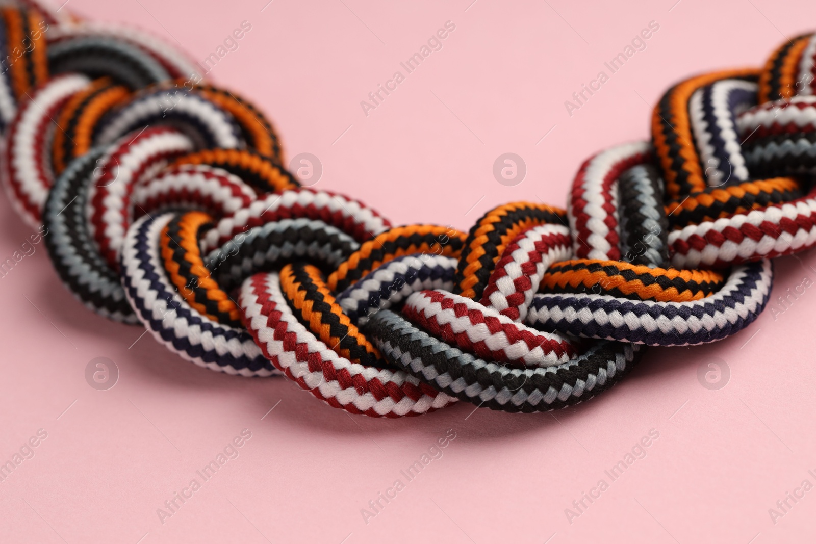 Photo of Braided colorful ropes on light pink background, closeup. Unity concept