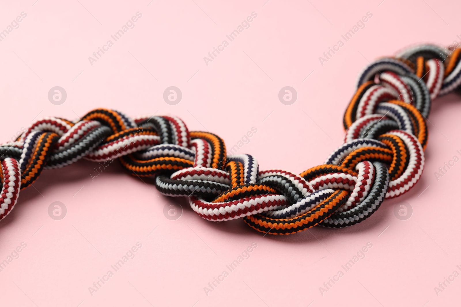 Photo of Braided colorful ropes on light pink background, closeup. Unity concept