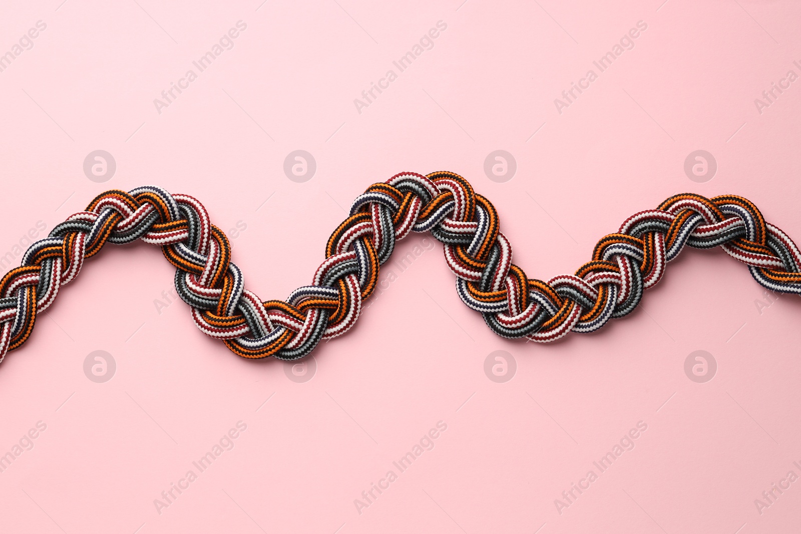 Photo of Braided colorful ropes on light pink background, top view. Unity concept