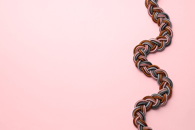 Photo of Braided colorful ropes on light pink background, top view with space for text. Unity concept