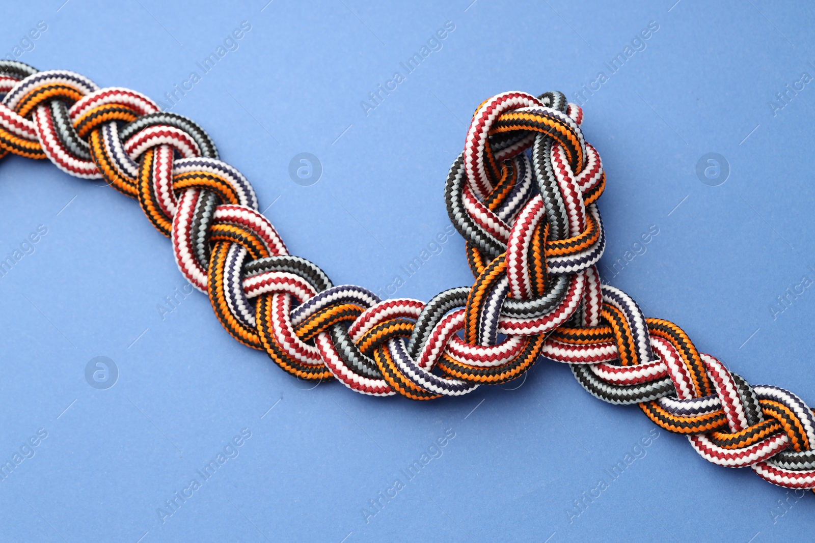 Photo of Braided colorful ropes on blue background, top view. Unity concept