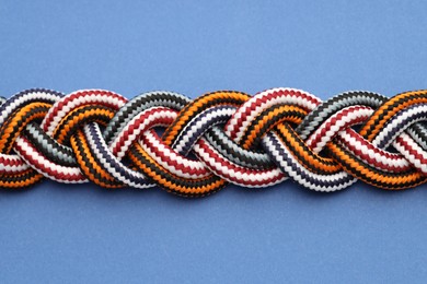 Photo of Braided colorful ropes on blue background, closeup. Unity concept