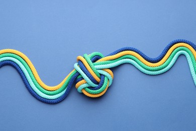 Photo of Colorful ropes tied in knot on blue background, top view. Unity concept