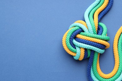 Photo of Colorful ropes tied in knot on blue background, top view with space for text. Unity concept