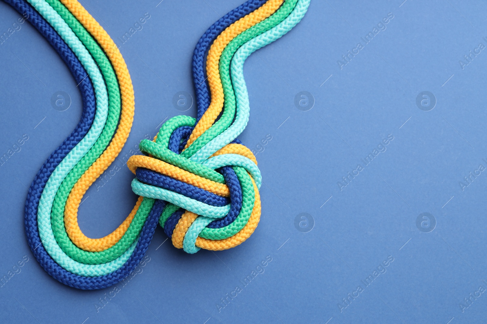 Photo of Colorful ropes tied in knot on blue background, top view with space for text. Unity concept