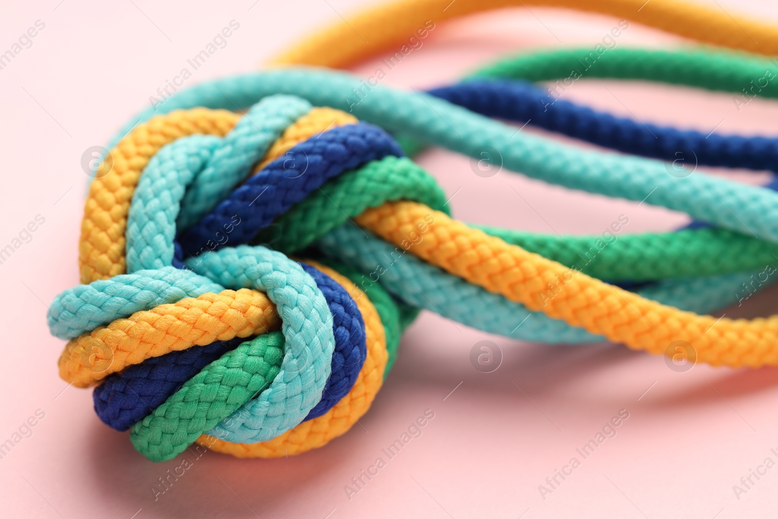 Photo of Colorful ropes tied in knot on light pink background, closeup. Unity concept