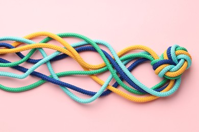 Colorful ropes tied in knot on light pink background, top view. Unity concept