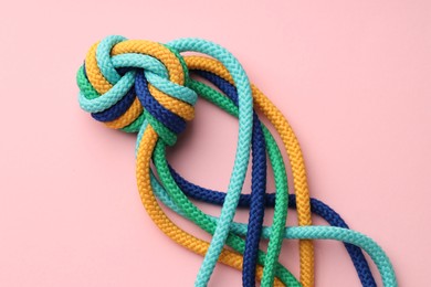 Photo of Colorful ropes tied in knot on light pink background, top view. Unity concept