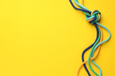 Photo of Colorful ropes tied in knot on yellow background, top view. Unity concept