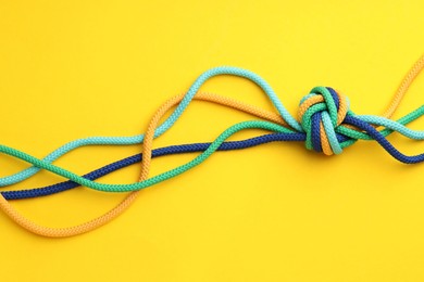 Photo of Colorful ropes tied in knot on yellow background, top view. Unity concept