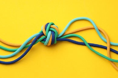 Photo of Colorful ropes tied in knot on yellow background, top view. Unity concept