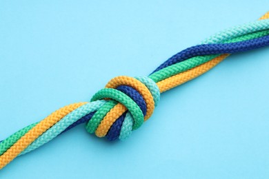 Photo of Colorful ropes tied in knot on light blue background, closeup. Unity concept