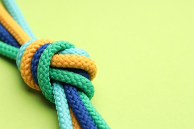 Photo of Colorful ropes tied in knot on light green background, closeup. Unity concept