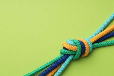 Photo of Colorful ropes tied in knot on light green background, top view with space for text. Unity concept