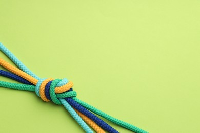 Photo of Colorful ropes tied in knot on light green background, top view with space for text. Unity concept