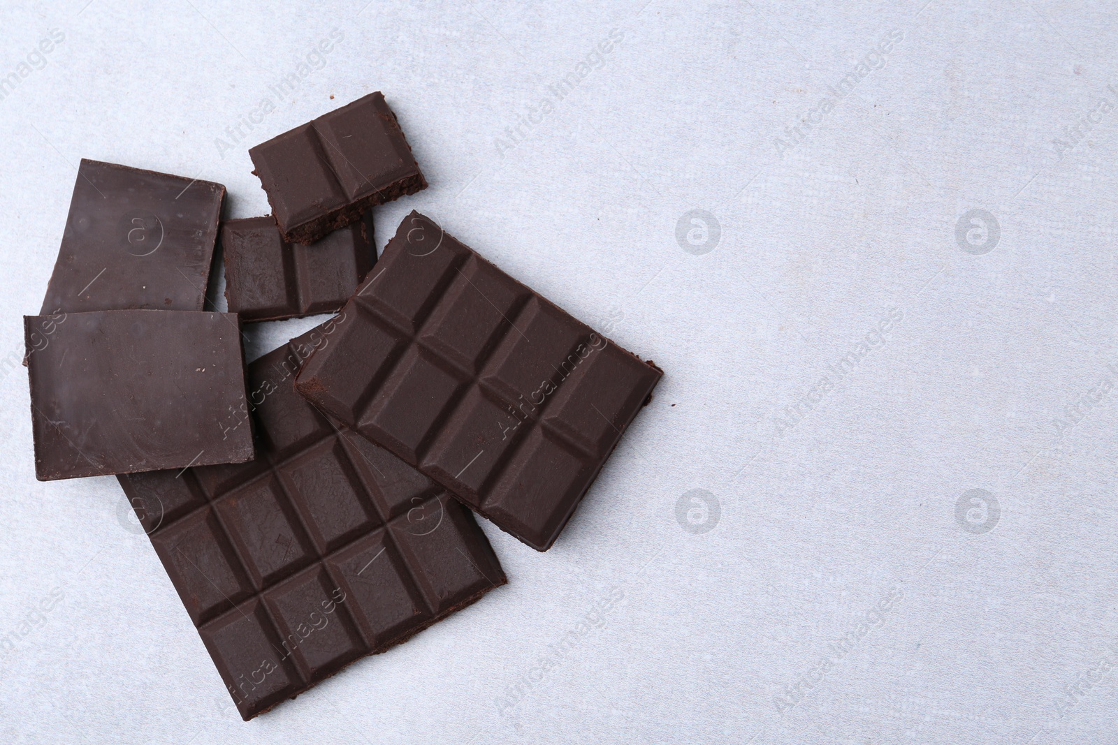 Photo of Pieces of delicious dark chocolate on light table, top view. Space for text