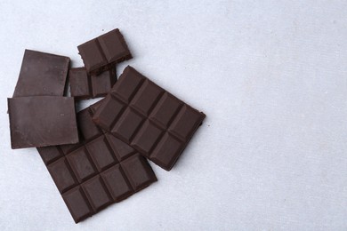 Photo of Pieces of delicious dark chocolate on light table, top view. Space for text