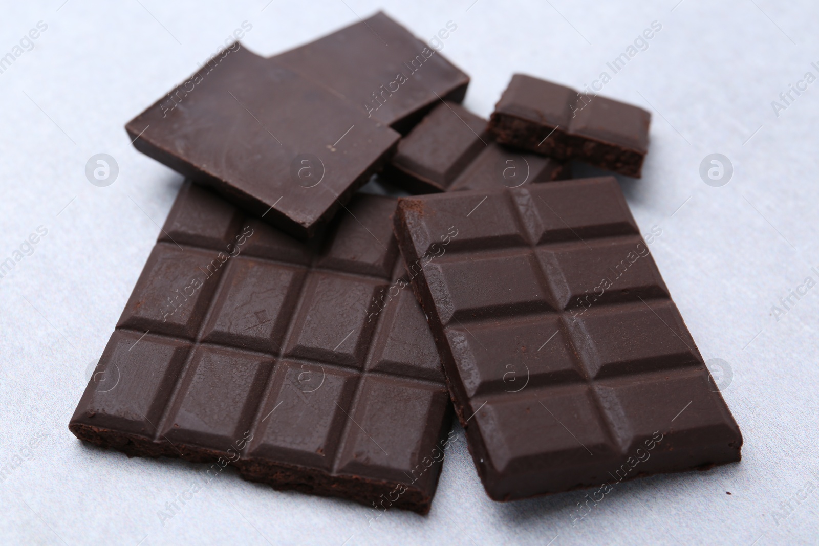 Photo of Pieces of delicious dark chocolate on light table, closeup