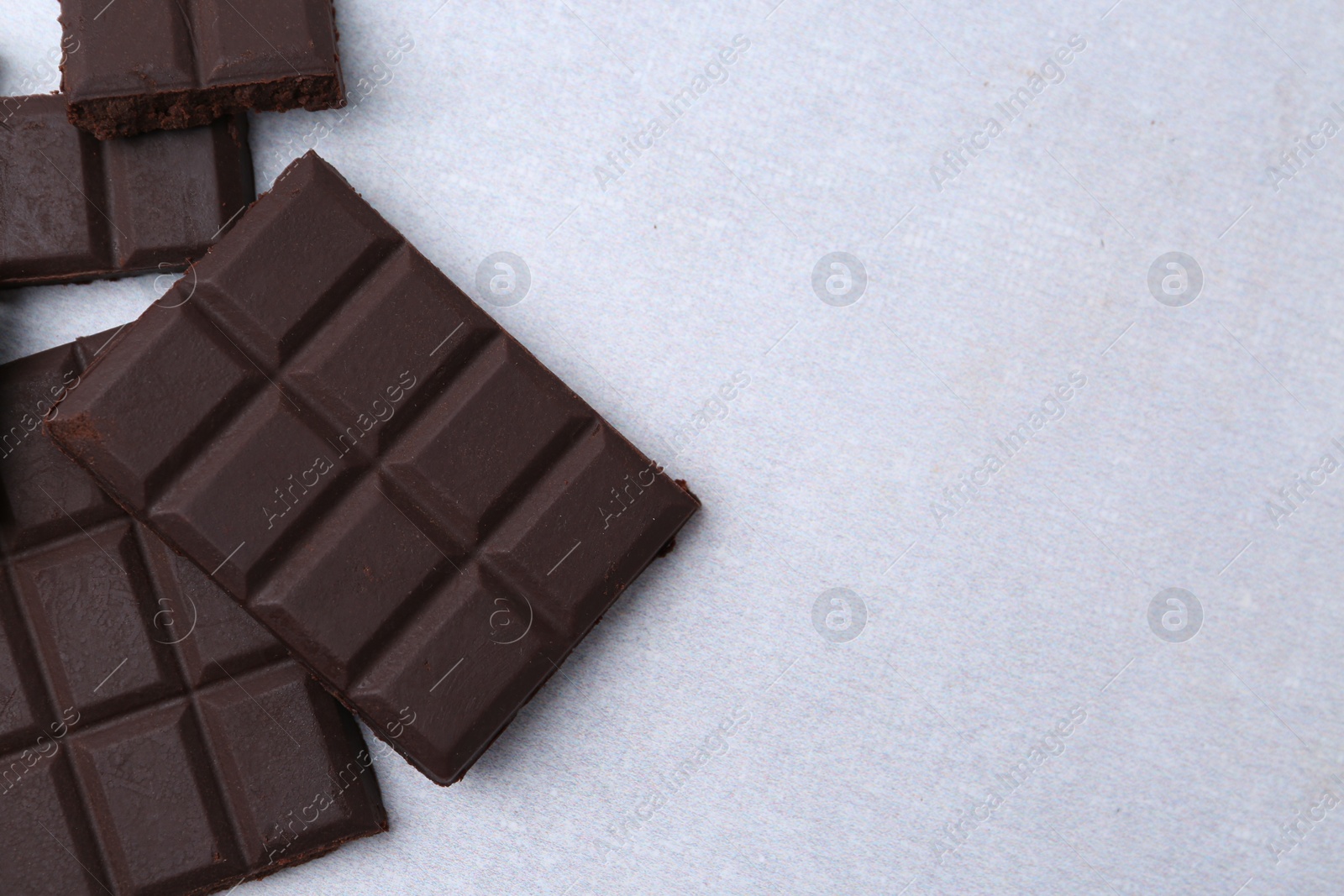 Photo of Pieces of delicious dark chocolate on light table, top view. Space for text