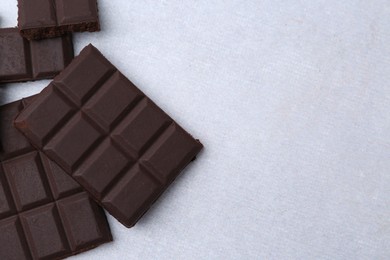 Photo of Pieces of delicious dark chocolate on light table, top view. Space for text