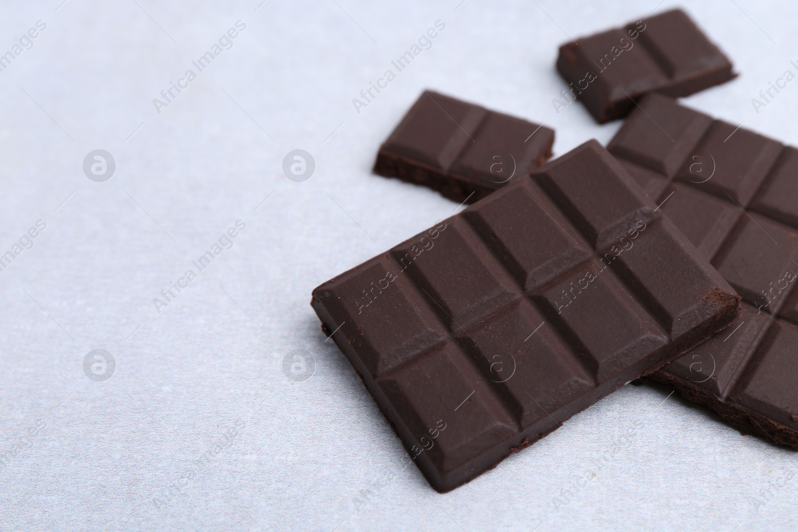 Photo of Pieces of delicious dark chocolate on light table, closeup. Space for text