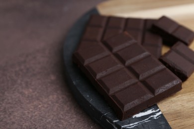 Photo of Pieces of delicious dark chocolate on brown table, closeup. Space for text