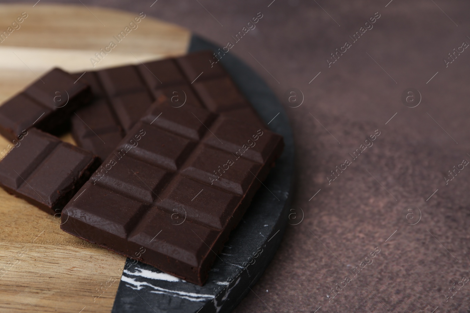 Photo of Pieces of delicious dark chocolate on brown table, closeup. Space for text