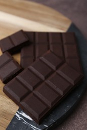 Photo of Pieces of delicious dark chocolate on brown table, closeup