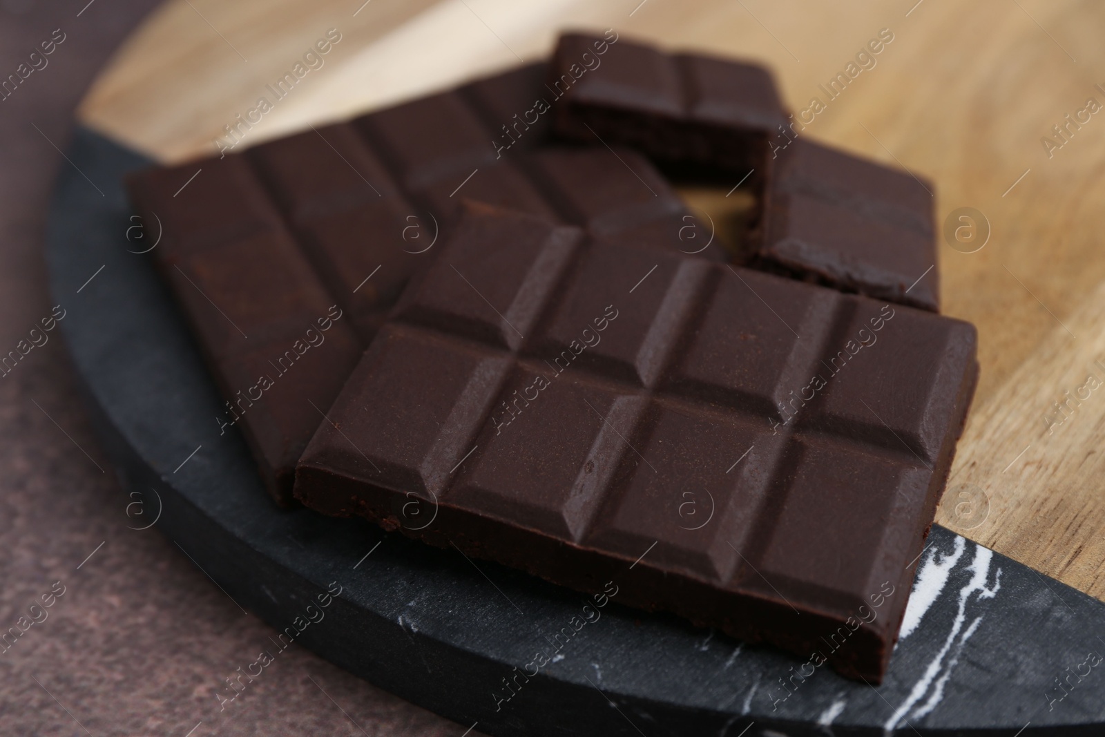 Photo of Pieces of delicious dark chocolate on brown table, closeup