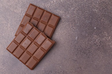 Photo of Pieces of delicious milk chocolate on brown table, top view. Space for text