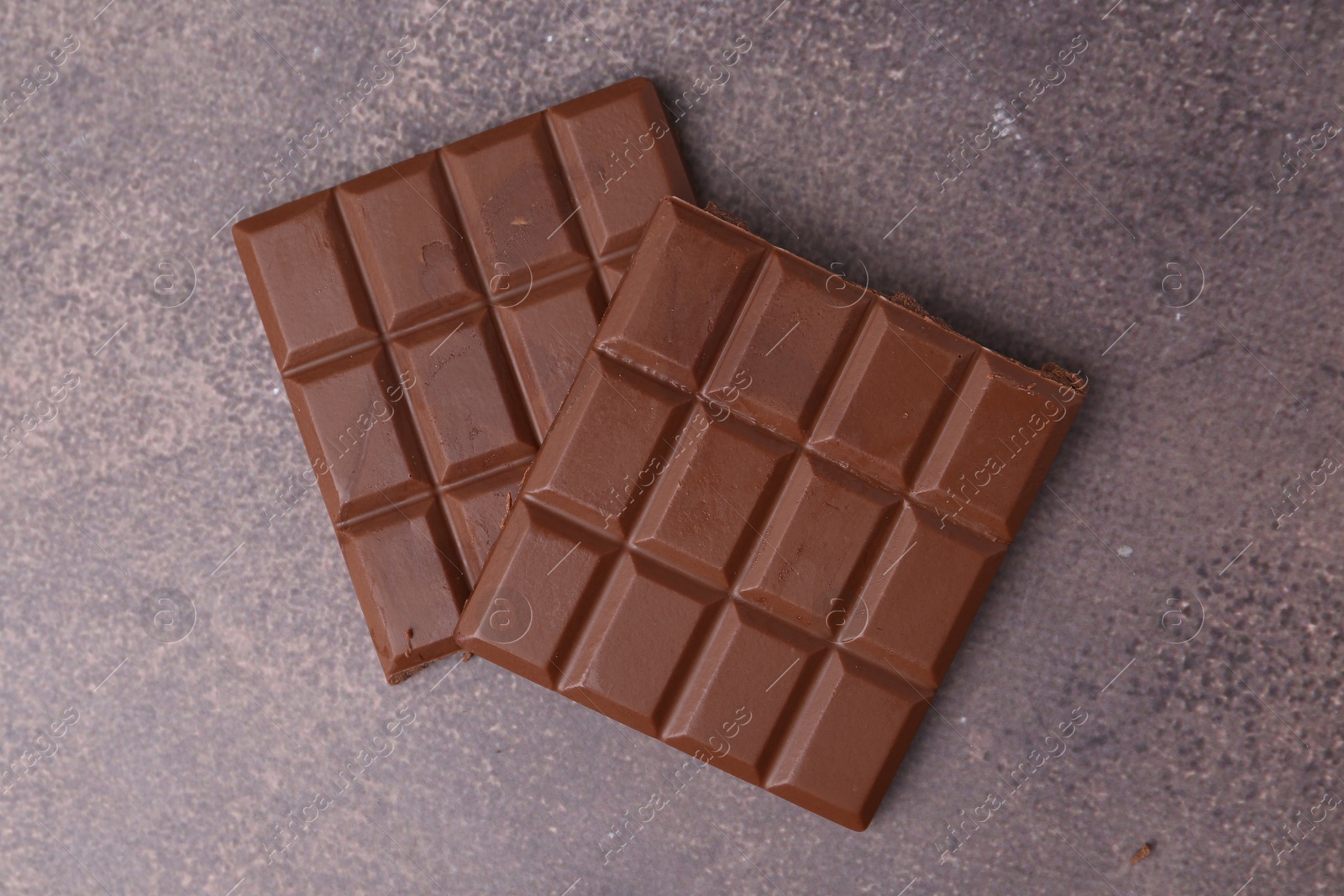 Photo of Pieces of delicious milk chocolate on brown table, top view