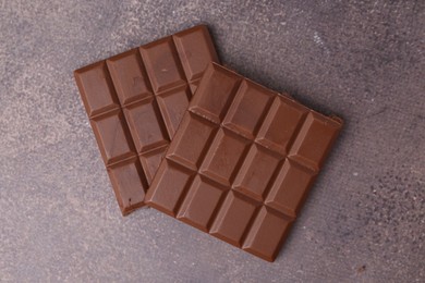 Photo of Pieces of delicious milk chocolate on brown table, top view