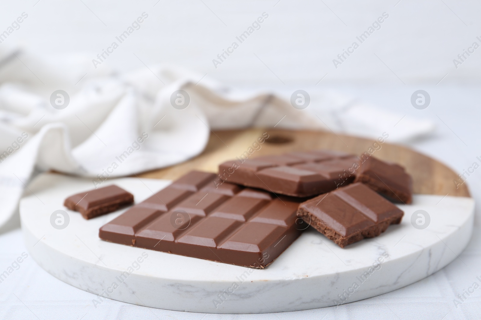 Photo of Pieces of delicious milk chocolate on white tiled table, closeup