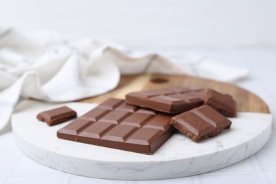 Photo of Pieces of delicious milk chocolate on white tiled table, closeup