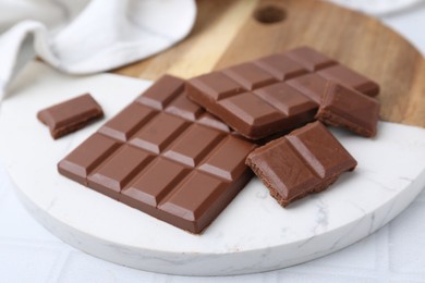 Photo of Pieces of delicious milk chocolate on white tiled table, closeup