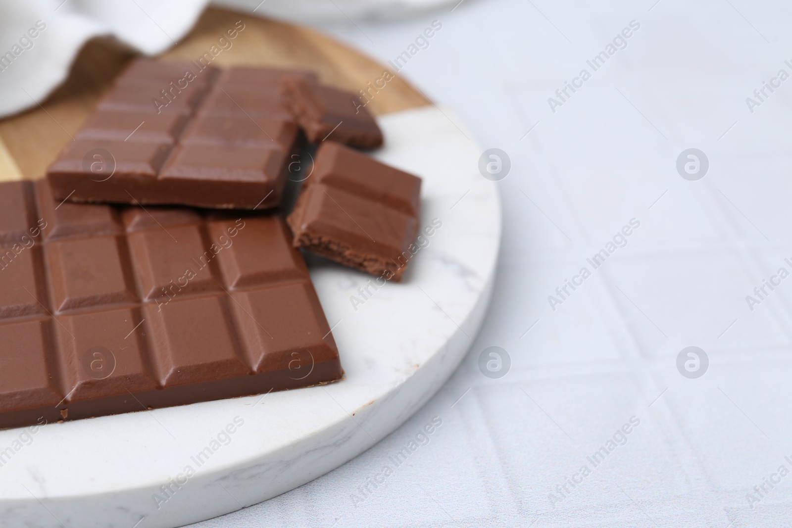 Photo of Pieces of delicious milk chocolate on white tiled table, closeup. Space for text