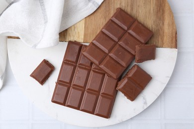 Photo of Pieces of delicious milk chocolate on white tiled table, top view