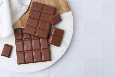 Photo of Pieces of delicious milk chocolate on white tiled table, top view. Space for text