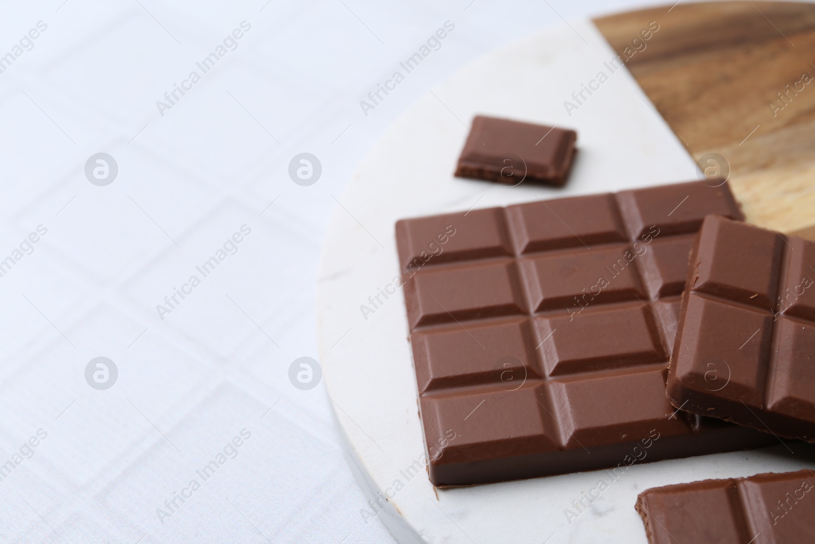 Photo of Pieces of delicious milk chocolate on white tiled table, closeup. Space for text