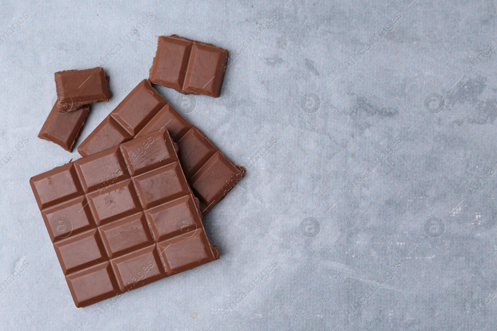 Photo of Pieces of delicious milk chocolate on grey table, top view. Space for text