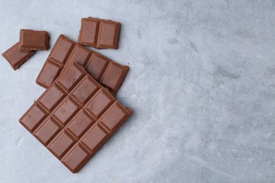 Photo of Pieces of delicious milk chocolate on grey table, top view. Space for text