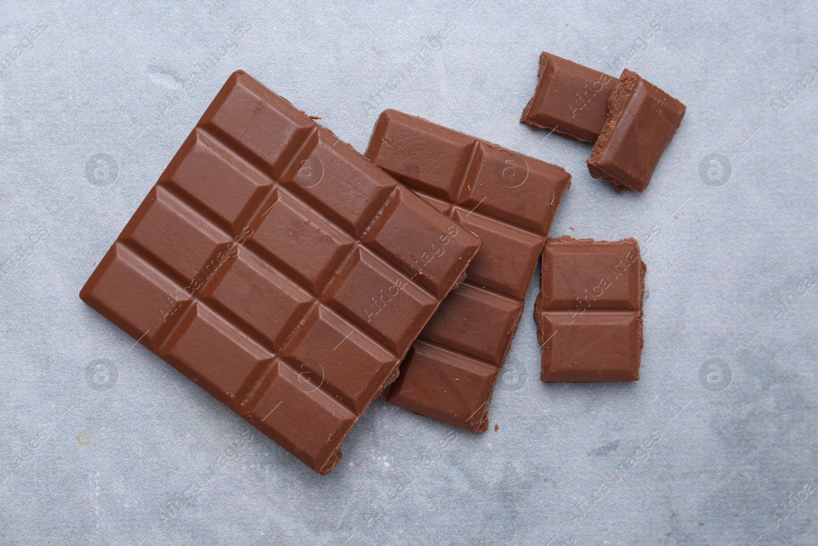 Photo of Pieces of delicious milk chocolate on grey table, top view