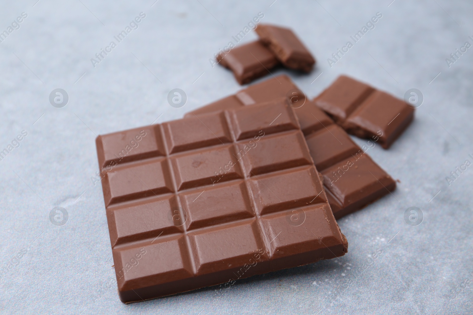 Photo of Pieces of delicious milk chocolate on grey table, closeup