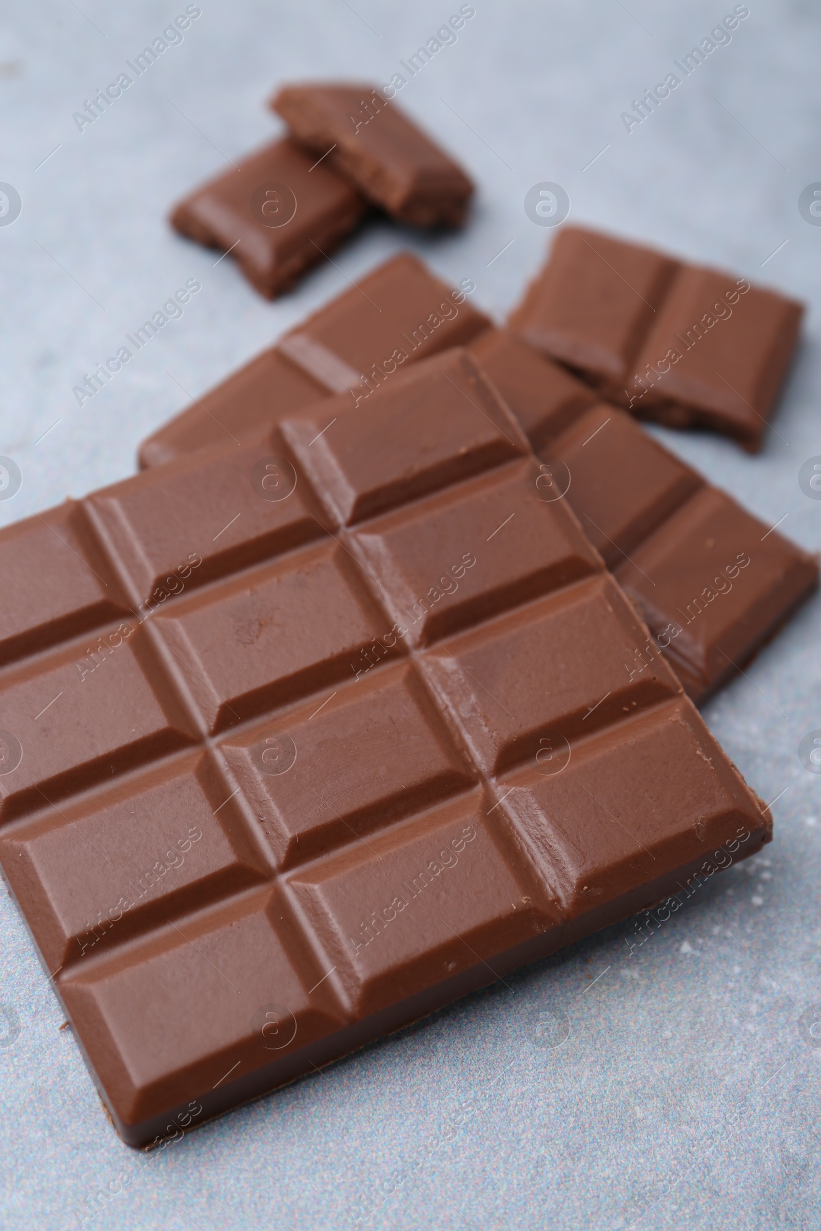 Photo of Pieces of delicious milk chocolate on grey table, closeup